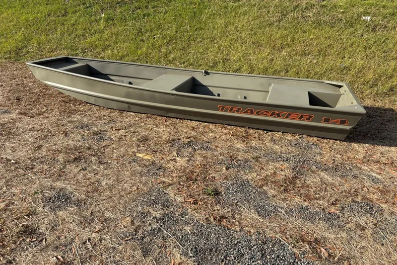 Slide: The Image of 2026 Tracker Grizzly 14 Jon boat on dry grass, showcasing its sturdy design. - 2