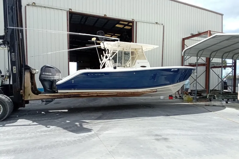 Slide: The Image of 2014 Cobia 296 Center Console boat on forklift, blue hull, Yamaha engine, in front of warehouse. - 50