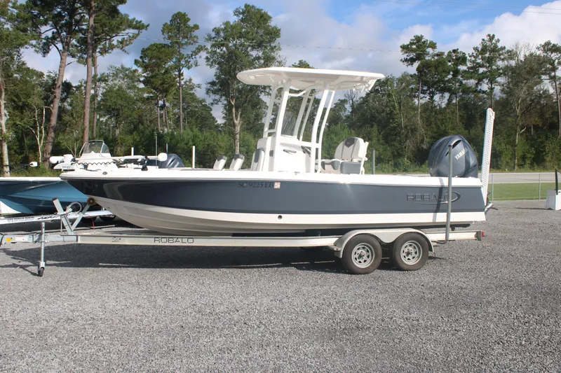 The Image of 2023 Robalo 226 Cayman boat on trailer, parked outdoors with trees in background. - 0