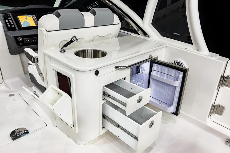 Slide: The Image of 2026 Chaparral 310 OSX boat interior with sink, storage drawers, and open mini fridge. - 7