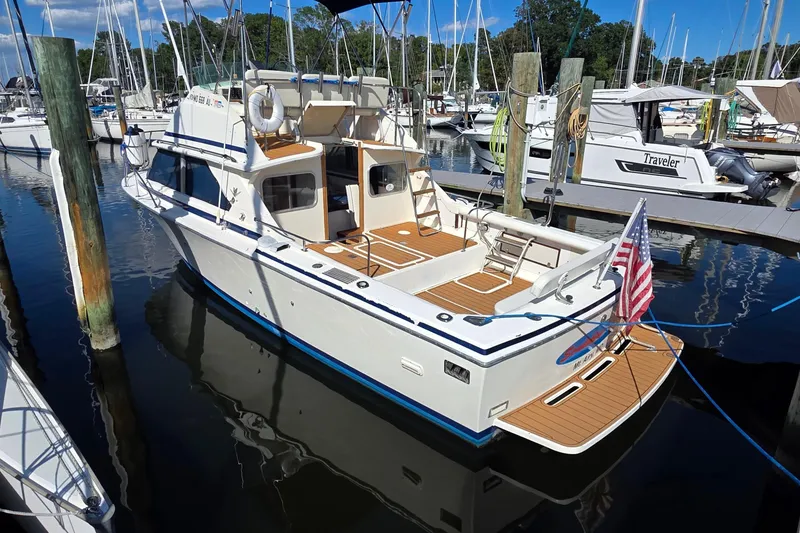 Slide: The Image of 1983 Bertram 28 Flybridge Cruiser docked at marina, featuring American flag and wooden deck. - 3