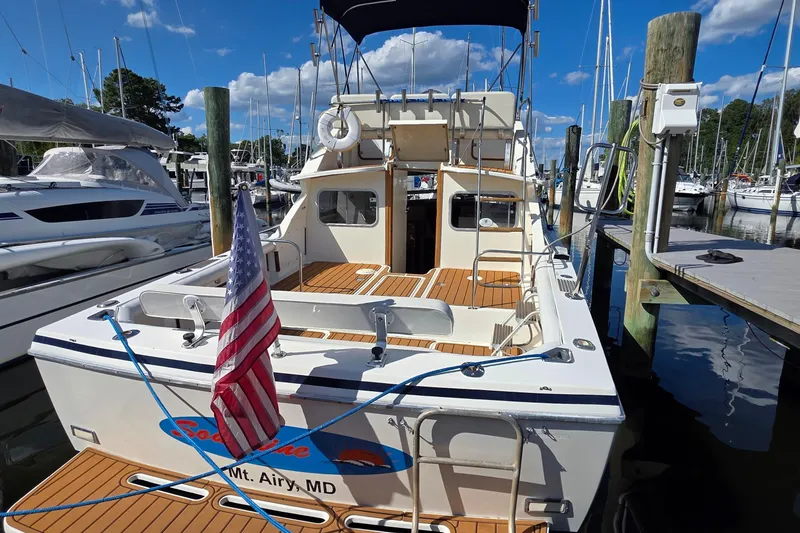 Slide: The Image of 1983 Bertram 28 Flybridge Cruiser docked, featuring American flag and wooden deck. - 5