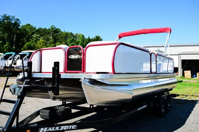 Slide: The Image of 2023 Aloha Pontoon Mahalo 23 boat on trailer, red and white design, outdoor setting. - 2