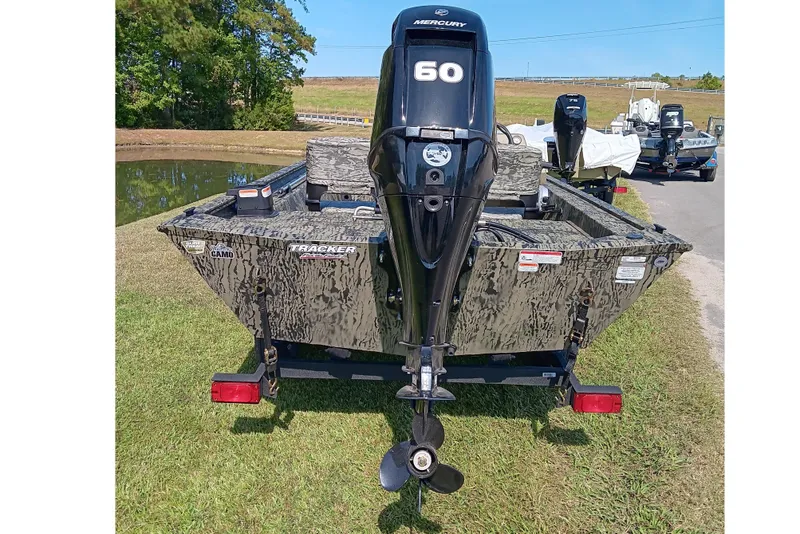 Slide: The Image of 2026 Tracker Grizzly 1754 SC boat with Mercury 60 engine, camo design, parked near a pond. - 4