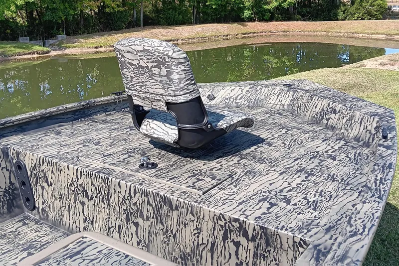 Slide: The Image of 2026 Tracker Grizzly 1754 SC boat with camouflage design by a pond. - 7