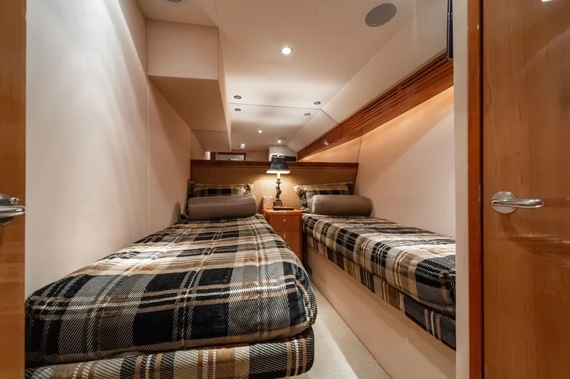 Slide: The Image of The 2008 Hatteras 64 Motor Yacht cabin features two single beds with plaid covers and a nightstand. - 17
