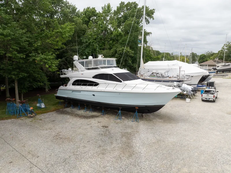 The Image of A 2008 Hatteras 64 Motor Yacht is on a dry dock, surrounded by trees and other boats. - 0