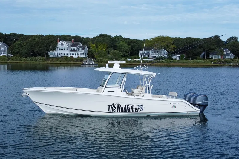 The Image of 2015 Cobia 344 Center Console boat on calm water near coastal homes. - 0