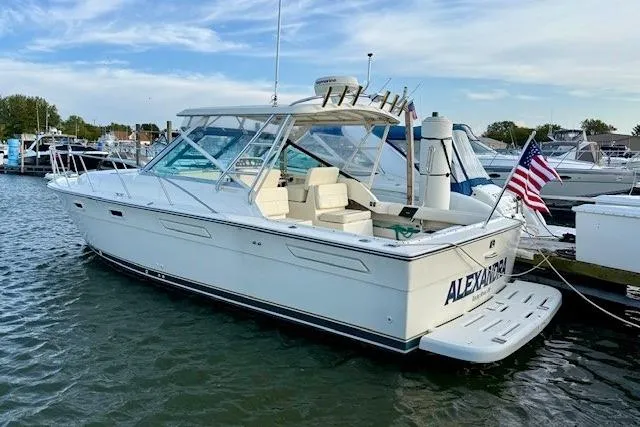 Slide: The Image of 1996 Pursuit 3100 Offshore cabin with wood table, beige seating, and control panel. - 3