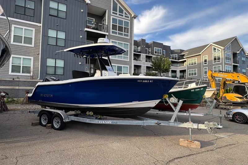 Slide: The Image of 2020 Blackfin 212 CC boat on trailer, parked near modern buildings. - 6
