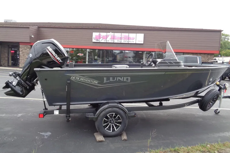 Slide: The Image of 2026 Lund 1675 Adventure SS boat with Mercury engine on trailer, parked outside a store. - 6