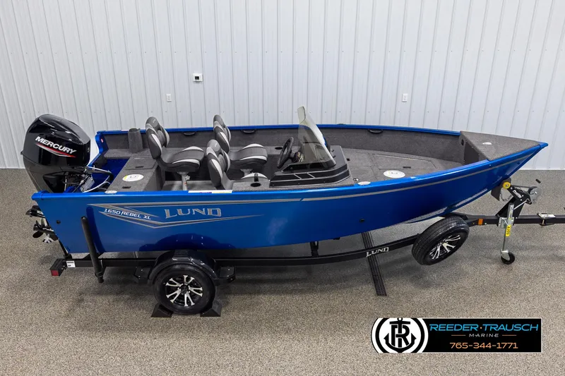 Slide: The Image of 2025 Lund Rebel XL SS boat with Mercury engine on trailer, displayed indoors. - 1
