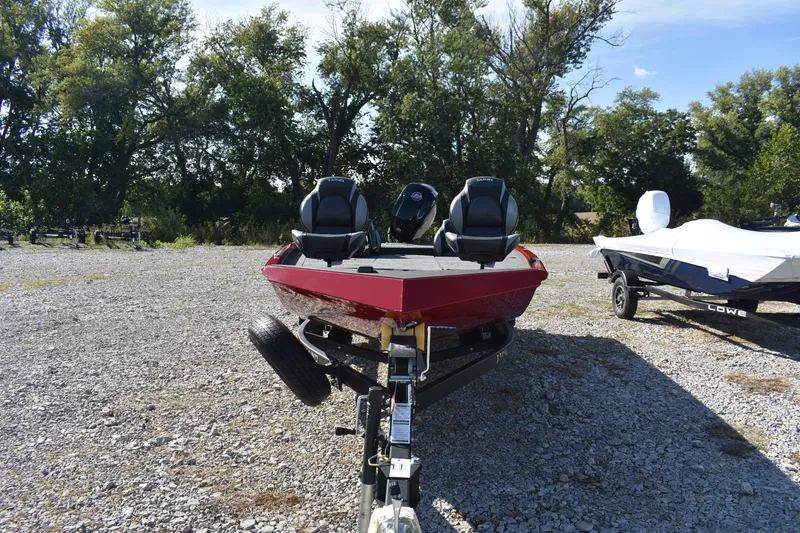 Slide: The Image of 2026 Lund 1875 Renegade boat on trailer, parked on gravel lot with trees in background. - 4
