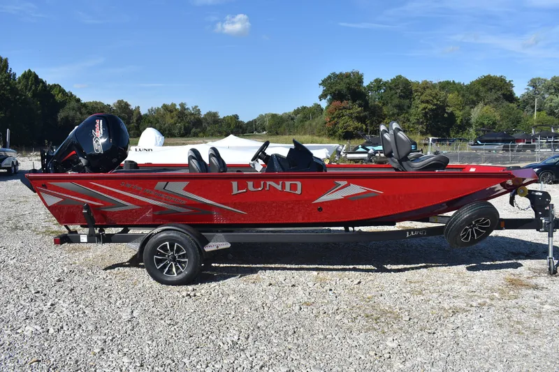 Slide: The Image of 2026 Lund 1875 Renegade boat in vibrant red, parked on gravel under a clear blue sky. - 5