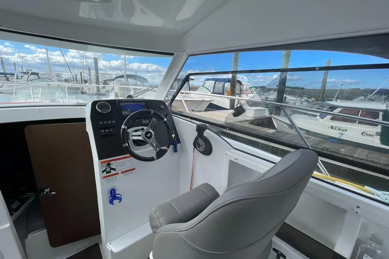 Slide: The Image of Interior view of 2020 Beneteau Antares 23 boat cockpit with steering wheel and marina background. - 10