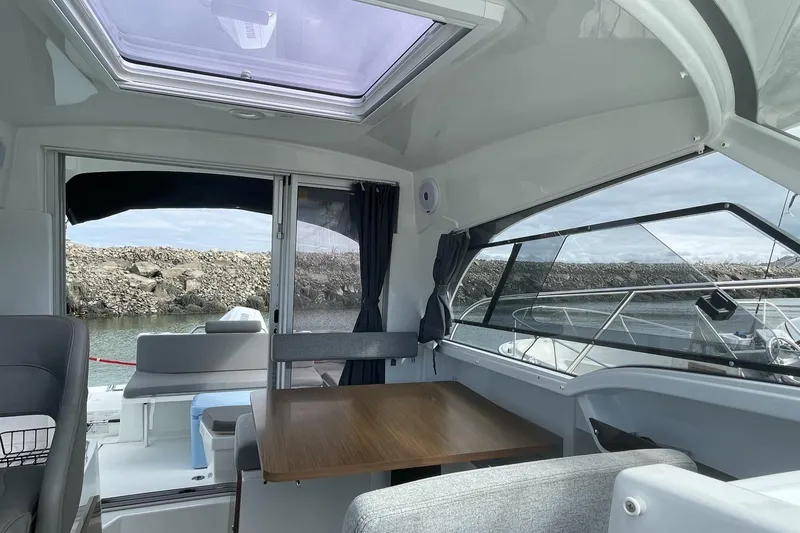 Slide: The Image of Interior of 2020 Beneteau Antares 23 boat with seating and table, docked by rocky shore. - 11