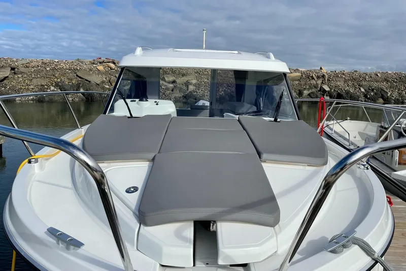 Slide: The Image of 2020 Beneteau Antares 23 boat with cushioned deck, docked by rocky shoreline. - 20