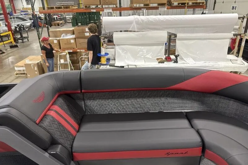 Slide: The Image of 2026 Bennington 24 MFBSF boat interior with red and gray seating in a factory setting. - 16