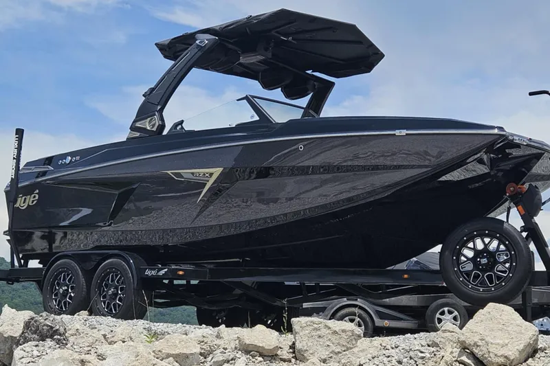 The Image of 2025 Tigé 22RZX boat on trailer, sleek black design, parked on rocky terrain. - 1