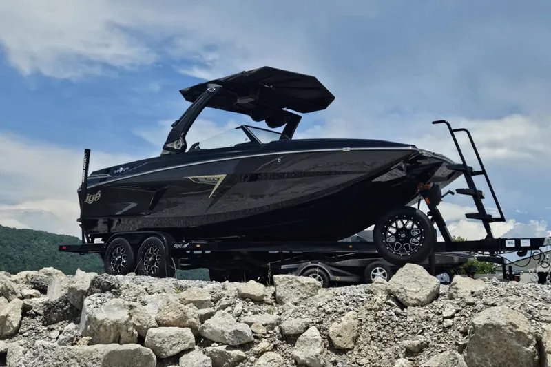 Slide: The Image of 2025 Tigé 22RZX boat on trailer, parked on rocky terrain under a cloudy sky. - 9