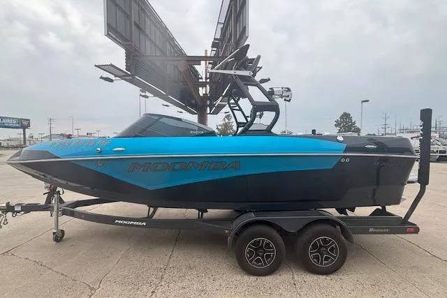 Slide: The Image of 2022 Moomba Kaiyen boat on trailer, blue and black design, parked outdoors. - 1