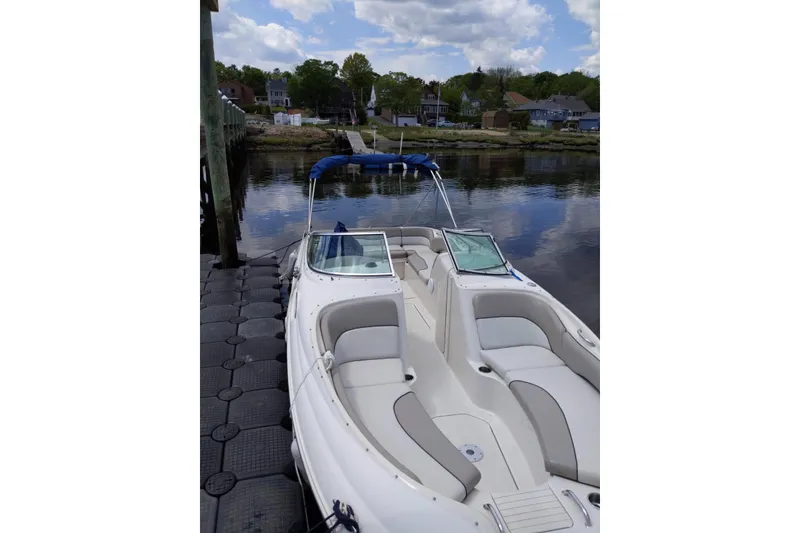 Slide: The Image of 2002 Sea Ray 240 Sundeck boat docked by calm waters, featuring spacious seating. - 2
