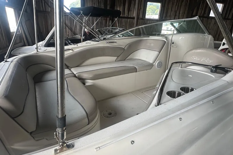 Slide: The Image of 2002 Sea Ray 240 Sundeck interior with beige seating and cup holders in a wooden boathouse. - 7
