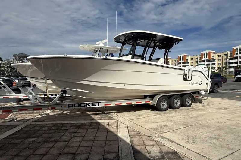 The Image of 2023 Robalo R302 Center Console boat on a trailer in a parking lot. - 1