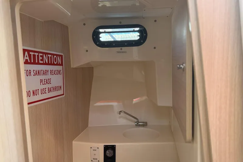 Slide: The Image of 2024 Bayliner Trophy T25 Pilothouse bathroom with warning sign, sink, and porthole window. - 53