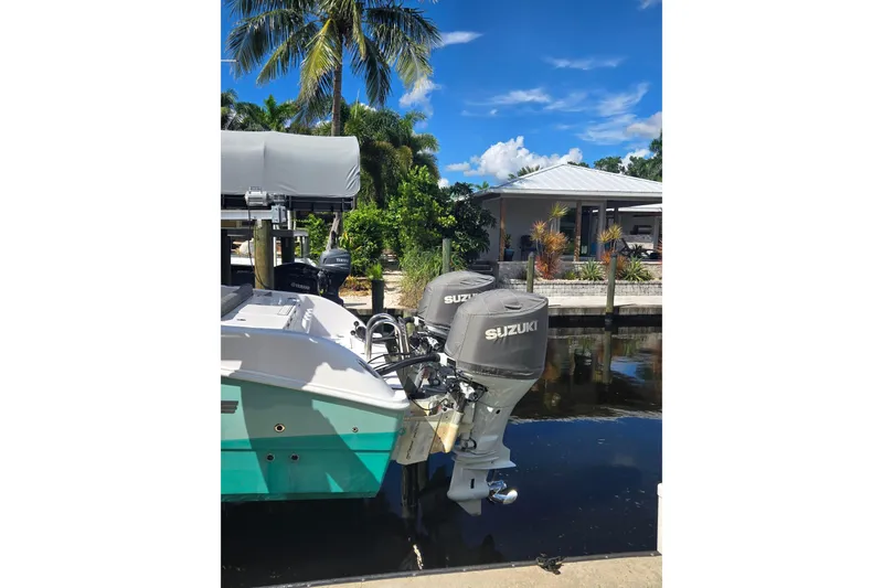Slide: The Image of 2024 Twin Vee 240 GFX CC boat with Suzuki outboard motors docked by a tropical waterfront. - 13