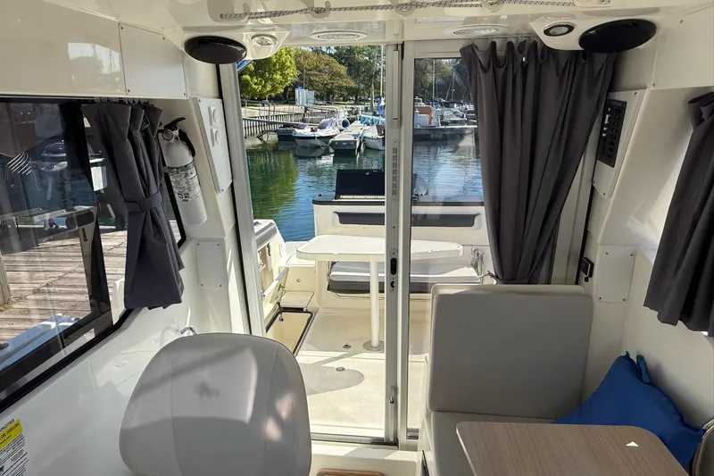 Slide: The Image of 2024 Bayliner Trophy T25 Pilothouse interior with seating, table, and marina view. - 41