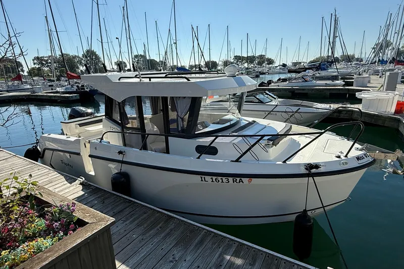 Slide: The Image of 2024 Bayliner Trophy T25 Pilothouse boat docked in a marina, surrounded by sailboats. - 8