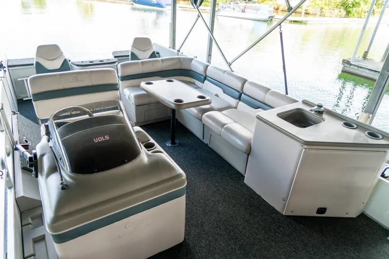Slide: The Image of 2000 Sun Tracker Fishin' Barge 25 interior with seating, table, and sink on a calm lake. - 10