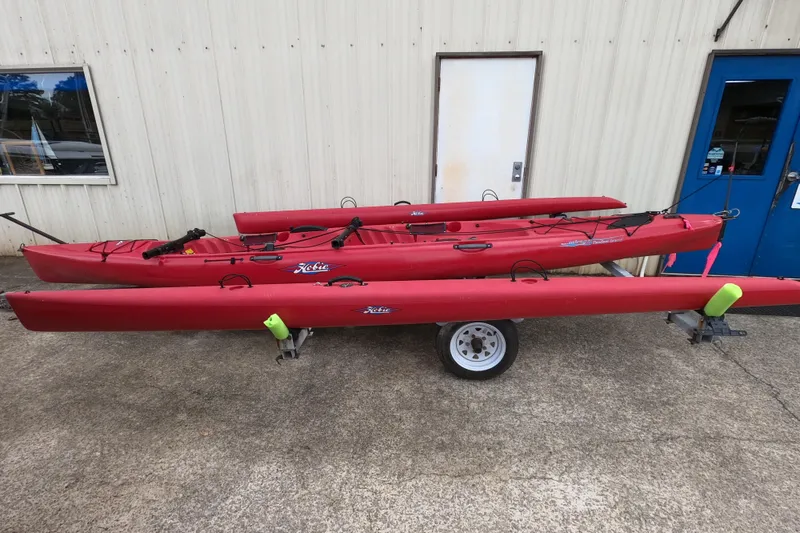 The Image of Red 2012 Hobie Mirage Tandem Island kayaks on a trailer outside a building. - 0