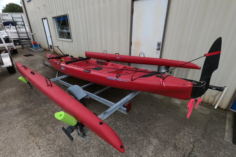 Slide: The Image of 2012 Hobie Mirage Tandem Island kayak on trailer, red with outriggers, parked by building. - 3