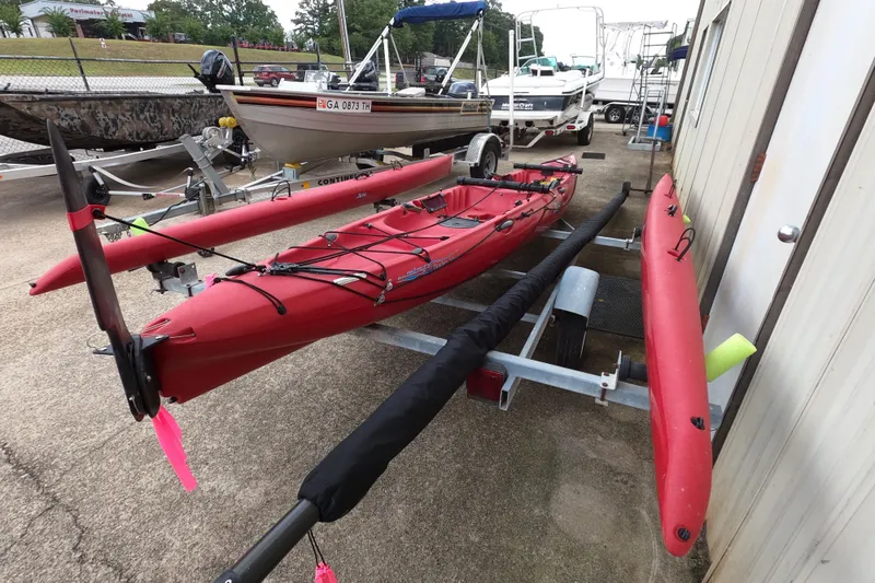 Slide: The Image of Red 2012 Hobie Mirage Tandem Island kayak on trailer, parked near other boats. - 6