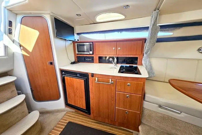 Slide: The Image of Interior of a 2008 Bayliner 320 boat featuring a compact kitchen with wood cabinetry. - 14
