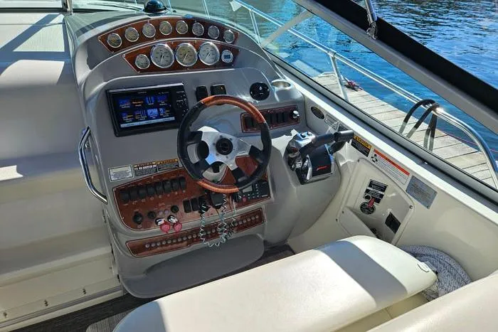 Slide: The Image of 2008 Bayliner 320 boat cockpit with steering wheel, control panel, and gauges by the water. - 5