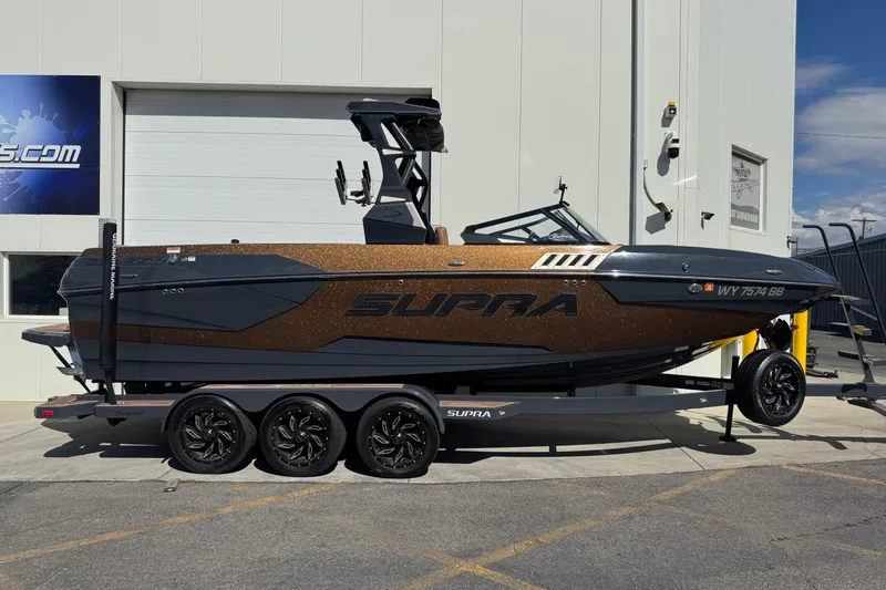 The Image of 2021 Supra SE 575 boat on trailer, parked outside a building under clear skies. - 0