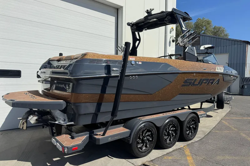Slide: The Image of 2021 Supra SE 575 boat on trailer, sleek design, parked outside a garage. - 1
