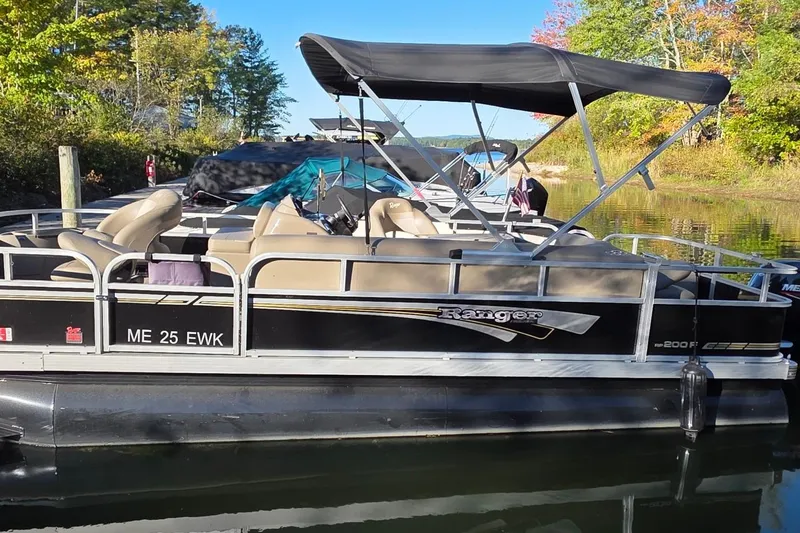 Slide: The Image of 2023 Ranger Reata 200F pontoon boat docked on a calm lake. - 14