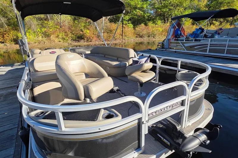 Slide: The Image of 2023 Ranger Reata 200F pontoon boat with beige seating, docked by a scenic lakeside. - 3