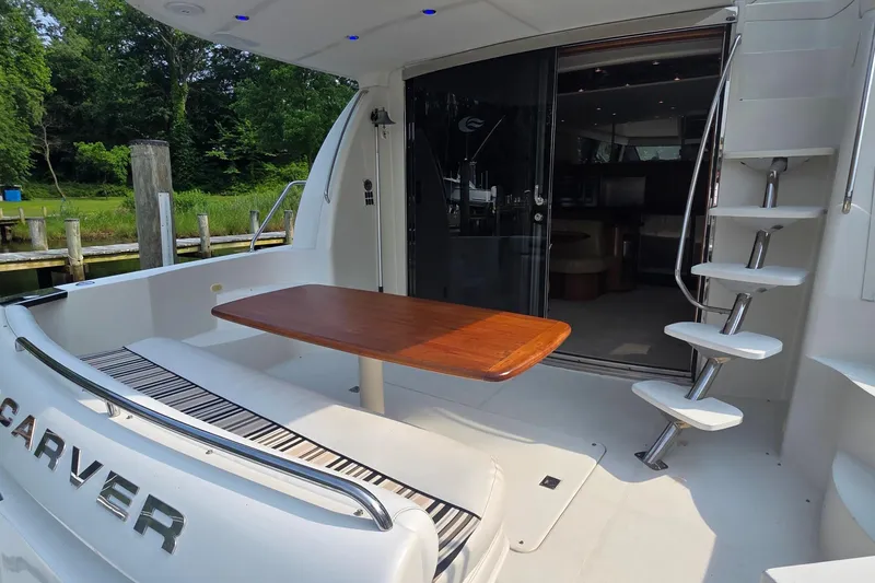 Slide: The Image of 2006 Carver 56 Voyager yacht deck with table and stairs, surrounded by lush greenery. - 10