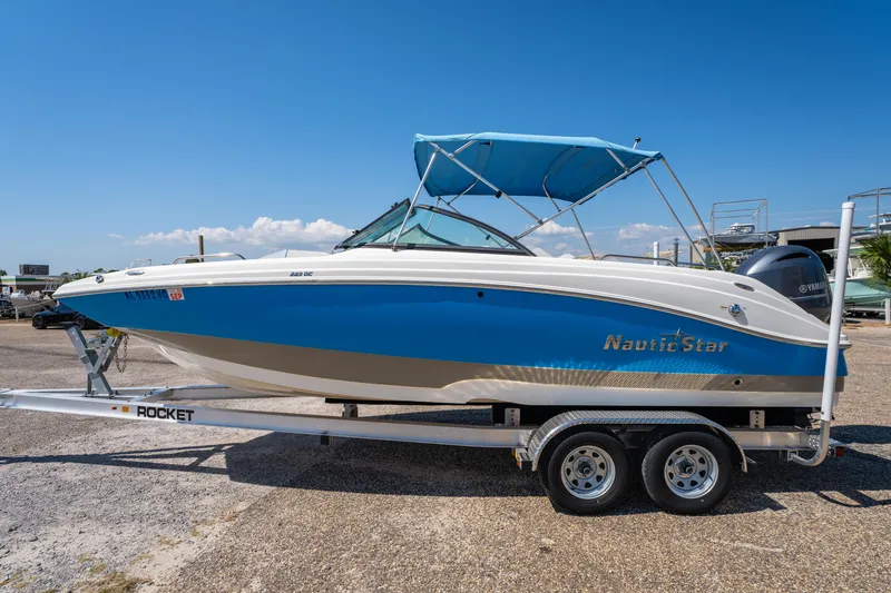 Slide: The Image of 2017 NauticStar 223DC Sport Deck boat on trailer, blue and white design, sunny day. - 1