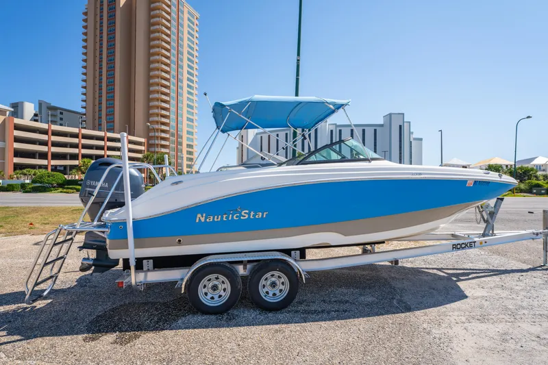 Slide: The Image of 2017 NauticStar 223DC Sport Deck boat on trailer, parked near tall buildings. - 2