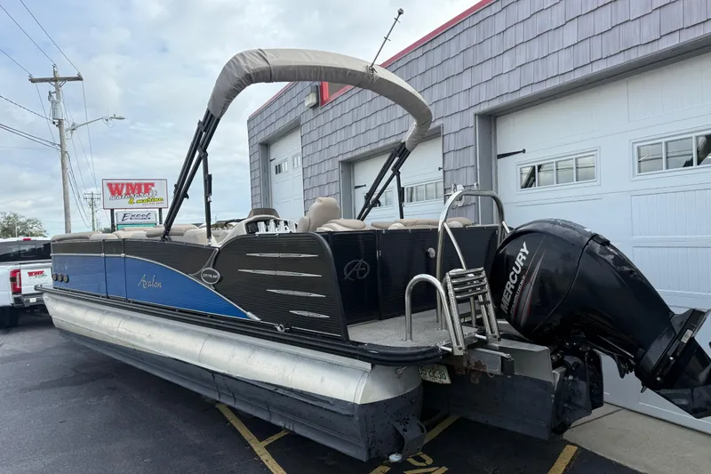 Slide: The Image of 2018 Avalon 2585 Catalina Elite Tri-toon boat with Mercury engine, parked outside a garage. - 6