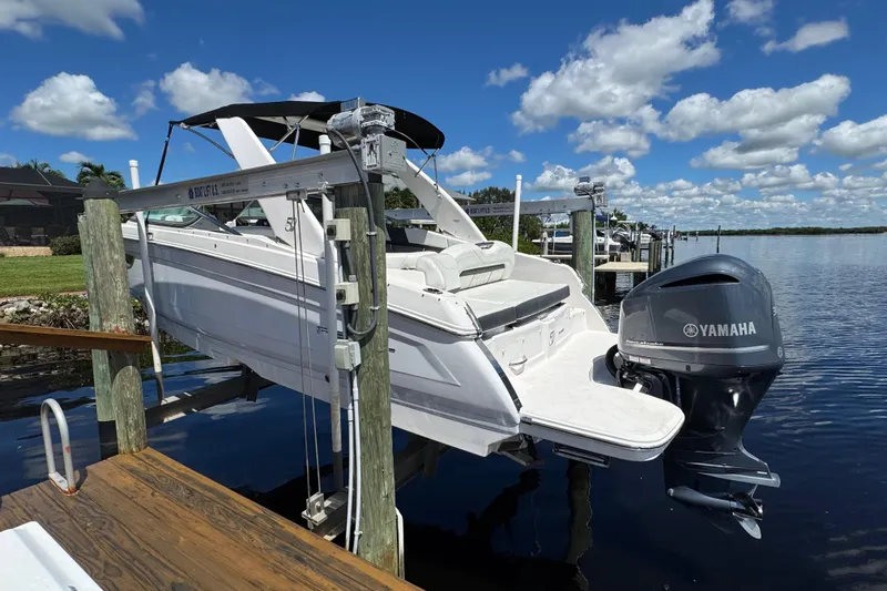 Slide: The Image of 2021 Regal 26 OBX boat with Yamaha outboard motor on a lift by the water. - 2