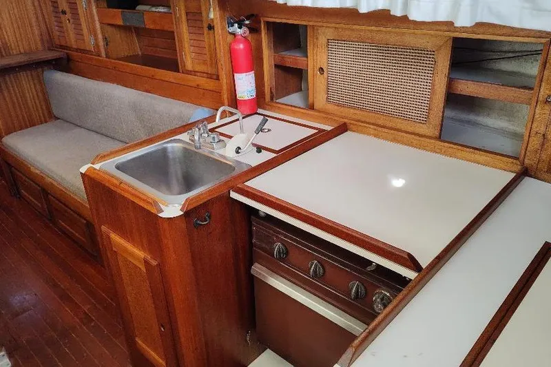 Slide: The Image of 1979 Bristol Yawl interior with wooden cabinetry, sink, stove, and seating area. - 18