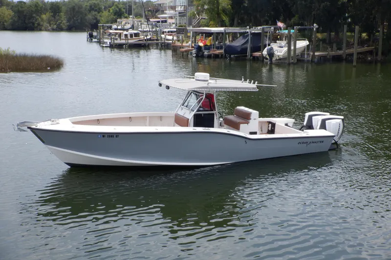 The Image of 1995 Ocean Master 31 Center Console boat on calm water, docked near a marina. - 0