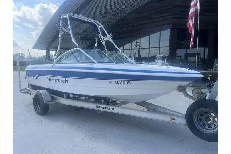 The Image of 1999 MasterCraft Prostar 205 boat on trailer, parked outdoors with American flag in background. - 0